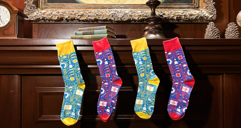 Four GitHub-branded socks in alternating colors hanging from a wooden mantel, like Christmas stockings.