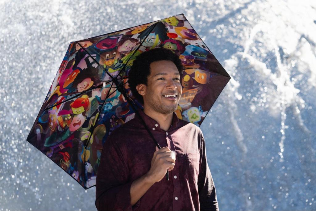 A smiling man stands underneath an open umbrella, the underside of which is printed with a collage of GitHub stickers.