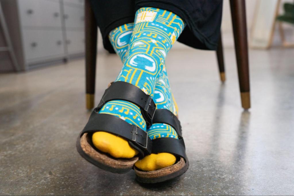 A pair of feet clad in blue and yellow GitHub-branded socks, worn with black Birkenstock sandals.