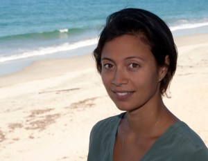 Headshot photograph of Kakani Katija. She is standing on a beach with the ocean visible behind her.