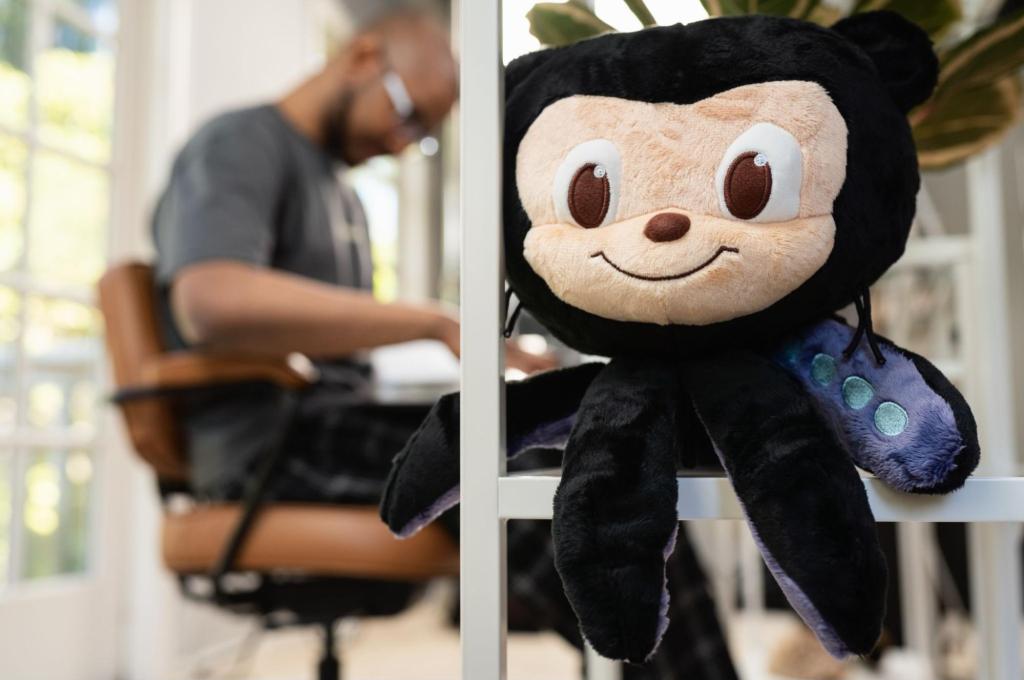 A smiling plush octocat toy is visible in the foreground of the photo, with a man working at a laptop slightly blurry in the background.