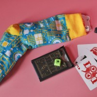 Yellow and blue sock with GitHub keycaps coming out the top and GitHub playing cards with Mona on a pink background.