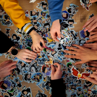 Several people's hands are reaching into a big pile of stickers on top of a table.