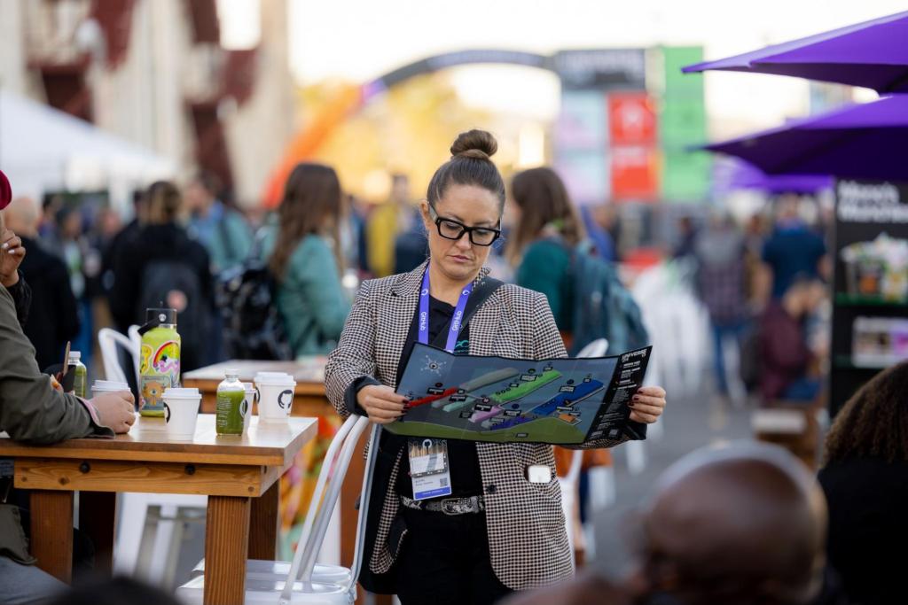 Conference attendee in checkered blazer reading event map in crowded exhibition hall.