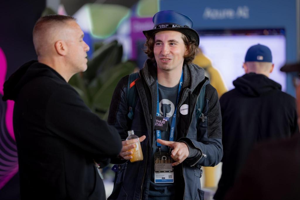 Two attendees having conversation at tech conference, one wearing GitHub Star tag and blue cap.